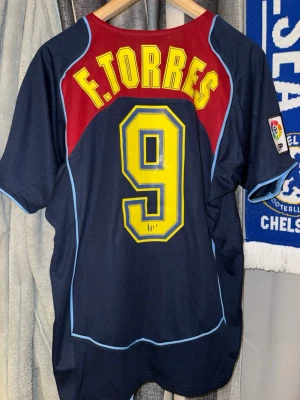 Atlético Madrid Spiderman tröja Torres - Mörkblå Atlético Madrid matchtröja med Spiderman-tryck på framsidan, officiellt klubbmärke och Nike-logga. På ryggen står F. Torres och nummer 9 i gult. Tröjan har röda och ljusblå detaljer samt La Liga-märke på ärmen. Perfekt för fotbollsfans!