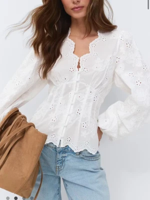 Vit broderad blus med spetskant från Gina  - Superfin vit blus med broderade blommor och hålbroderier. Blusen har långärmade puffärmar, figurnära passform och dekorativa knappar framtill. V-ringad hals med vågig spetskant och söt avslutning nedtill. Perfekt till jeans för en romantisk look. Endast testad!