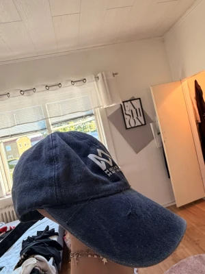 Blå Marcus & Martinus keps - Säljer en blå keps med böjd skärm och tryck Marcus & Martinus-logga framtill i vitt. Kepsen har klassisk passform och är tillverkad i ett mjukt tyg som ger en avslappnad look. Perfekt för dig som gillar streetwear och vill visa ditt stöd för Marcus & Martinus.