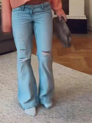 Ljusblå bootcut jeans med slitningar - Säljer ett par ljusblå bootcut jeans med slitningar över knäna. Jeansen har hög midja och klassisk femficksmodell. Perfekta för en avslappnad och trendig look.