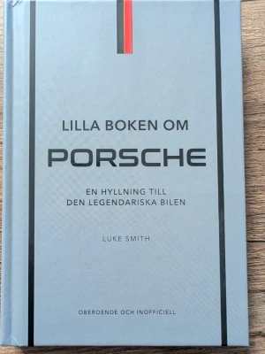 Lilla boken om Porsche - En snygg, grå hårdinbunden bok med titeln 'Lilla boken om Porsche' av Luke Smith. Boken är en hyllning till den legendariska bilen Porsche och har en stilren design med svarta och röda detaljer på omslaget. Perfekt för bilentusiaster och Porsche-fans.