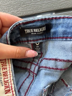 True Religion ljusblå jeans - Säljer ett par ljusblå jeans från True Religion med cool röd söm och broderad bakficka. Klassisk femficksmodell som passar till alla tillfällen. Jag säljer dessa då de inte passar! Bara att skriva om man undrar något! Det finns några små defekter. Jeansen är lite slitna vid hälen och är lagade lite under vänster framficka men jag upplever inte att det stör eller syns. 