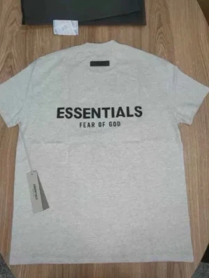 Grå Essentials Fear of God t-shirt - Snygg grå t-shirt från Essentials Fear of God med stor svart logga på ryggen. Klassisk passform och rund hals. Perfekt för dig som gillar streetwear och enkel stil.
