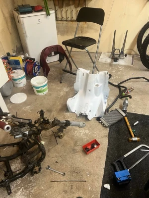 Mopedram och delar - Säljer en mopedram i metall tillsammans med flera lösa delar, inklusive vit plastkåpa och sadel med vinröda och vita detaljer. Perfekt för dig som vill bygga eller renovera en moped. Verktyg och smådelar syns också på bilderna.