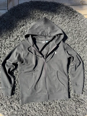 Svart hoodie från Polo Ralph Lauren - Svart hoodie från Polo Ralph Lauren med dragkedja framtill, två fickor och klassisk huva. Liten vit logga broderad på bröstet. Tillverkad i mjuk bomullsblandning som är skön att ha på sig. Perfekt för en chill och stilren look.