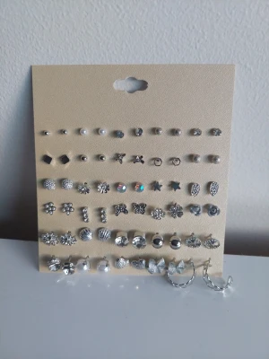 Set med 30 par silverfärgade örhängen - Stort set med 30 par örhängen i olika former som stjärnor, blommor, hjärtan, pärlor och hoops. Alla örhängen är i silverfärg och vissa har detaljer som glittrande stenar eller pärlor. Perfekt för dig som vill variera din stil med många olika motiv och former.