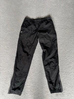 Svarta sportshorts från Lacoste - Svarta sportiga shorts från Lacoste med elastisk midja och klassisk krokodillogga på benet. Regular fit och vita detaljer längs sidorna. Perfekta för träning eller chill dagar. Materialet känns lätt och bekvämt.