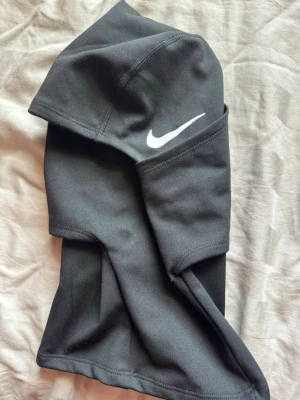 Svart balaclava från Nike Pro - Säljer en svart balaclava från Nike Pro med vit logga på sidan. Tillverkad i stretchigt funktionsmaterial som sitter tajt och bekvämt runt huvudet. Perfekt för träning utomhus eller kalla dagar. Snygg och sportig design med diskreta sömmar.