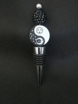 Vinkork/flaskkork med yin yang och solmotiv - Snygg handgjord vinkork/flaskkorki metall och svart plast med dekorativt yin yang-motiv, sol, måne och stjärnor. Toppen har en glittrande svart pärla och en silverfärgad kula. Perfekt accessoar till flaskor för dig som gillar unika detaljer.