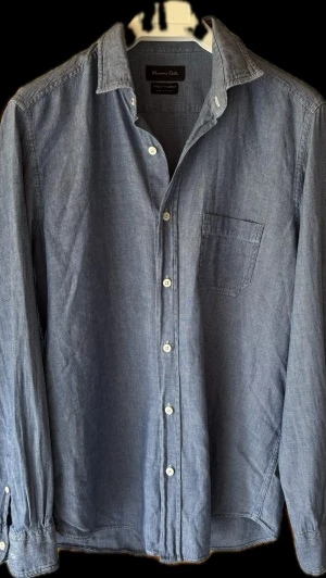 Massimo Dutti skjorta med knappar - Klassisk blå skjorta med lång ärm och vita knappar framtill. Skjortan har en bröstficka och enkel krage. Perfekt till jeans eller chinos för en avslappnad men snygg stil.