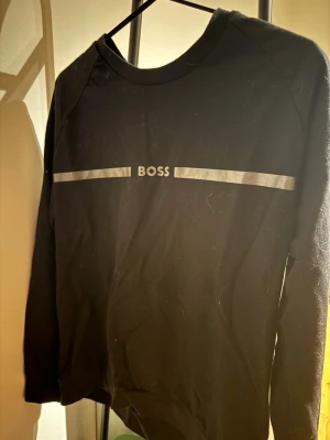 Boss Sweatshirt  - Svart långärmad tröja från BOSS med silverfärgade detaljer och logga framtill. Tröjan har en enkel och stilren design med rund halsringning. Perfekt för en clean och avslappnad look. PASSAR S OCH M