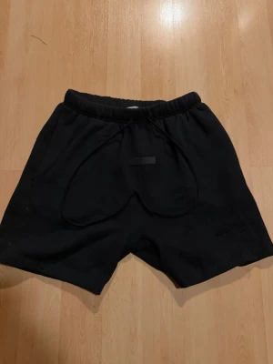 Svarta shorts från Essentials - Svarta shorts från Essentials Fear of God med elastisk midja och snörning. Klassisk loose fit och diskret logga framtill. Perfekta för en avslappnad och stilren look.