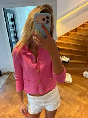 Rosa kofta med guldknappar - Snygg rosa kofta med trekvartsärm och dekorativa guldknappar framtill. Koftan har två små fickor och en rak, croppad passform. Perfekt för att addera färg till din outfit och passar lika bra till jeans som kjol.