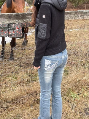 Blå bootcut jeans med broderad ficka - Snygga ljusblå bootcut jeans med slitningar och broderad detalj på bakfickan. Jeansen har en klassisk femficksmodell och sitter tajt över låren för att sedan bli vidare nedtill. Perfekta för en avslappnad och trendig look. De passar mig bra som e ungefär 177