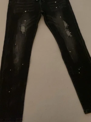 Svarta slitna skinny jeans - Säljer ett par svarta skinny jeans med slitningar på båda benen och vita färgstänk för en trendig look. Jeansen har smal passform och är tillverkade i denim med stretch. Perfekta för dig som gillar en edgy stil. 450 vid snabb beställning.