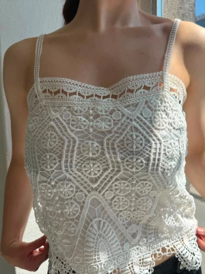 Vit spetslinnetopp med broderi - Säljer en superfin vit linnetopp med tunna axelband och detaljerat broderat spetsmönster. Toppen har en lätt genomskinlig look och fina virkade kanter upptill och nedtill. Perfekt för dig som gillar romantisk och bohemisk stil.