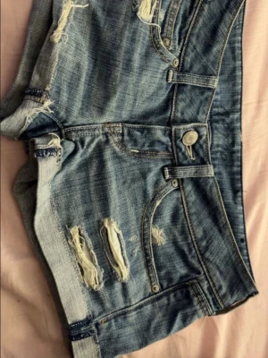 aerie jeans shorts - Säljer ett par blå jeansshorts med slitna detaljer och upprullade benslut. Shortsen har klassisk femficksdesign och knappgylf. Med midjemått 76cm. 