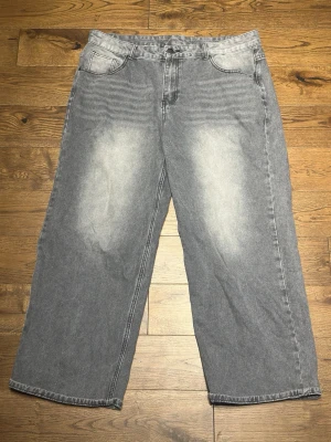 Gråa vida jeans med tvättade detaljer - Ett par gråa jeans med bred passform och tvättade detaljer framtill och baktill. Jeansen har klassisk femficksdesign och raka ben. Materialet är denim i bomull och färgen är ljusgrå med slitningar för en avslappnad look.