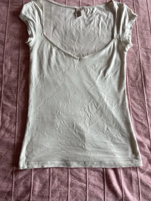 Vit v-ringad topp från H&M - Säljer en enkel och stilren vit topp från H&M med v-ringad hals och korta ärmar. Toppen är gjord i mjuk bomull och har en smickrande passform som sitter snyggt på kroppen. Perfekt att matcha med jeans eller kjol.