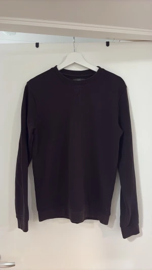 Mörkbrun sweatshirt från Dressmann - En basic mörkbrun sweatshirt från Dressmann med rund halsringning och ribbade muddar vid ärmslut och nederkant. Tillverkad i mjuk bomullsblandning och har en klassisk, avslappnad passform. Perfekt för dig som gillar stilrena och enkla plagg.