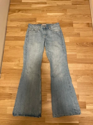 Ljusblå utsvängda jeans - Säljer ett par ljusblå jeans med utsvängda ben och rå kant längst ner. Klassisk femficksmodell med knapp och dragkedja framtill. Perfekta för dig som gillar retrostil och vill ha ett par riktigt snygga jeans i garderoben.