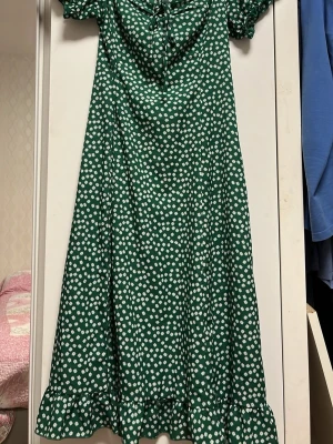 Grön blommig långklänning Shein - Grön långklänning från Shein med vitt blommönster, korta puffärmar och volangkant nertill. Klänningen har snörning vid bysten och är tillverkad i ett mjukt, lätt material som känns skönt mot huden.