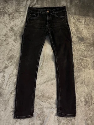 Svarta slim fit jeans från Kappahl - Snygga svarta slim fit jeans från Kappahl med klassisk femficksdesign och knappgylf. Jeansen har smal passform och är tillverkade i stretchigt material för extra komfort. Perfekta till en avslappnad grisch-look.  Vid frågor hör av dig och priset kan alltid diskuteras 