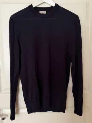 Mörkblå stickad tröja från H&M premium - En stilren mörkblå stickad tröja från H&M med rund halsringning och långa ärmar. Tröjan har ribbade muddar vid ärmslut och nederkant. Perfekt för lager på lager och enkel att matcha med olika outfits.