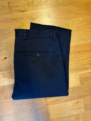These Glory Days T Ripley Elevated Chinos - Snygga mörkblå chinos med smal passform och klassiska bälteshällor. Byxorna har raka ben och stängs med knapp och dragkedja. Perfekta för en stilren och enkel look. Materialet ser ut att vara bomull eller bomullsblandning.