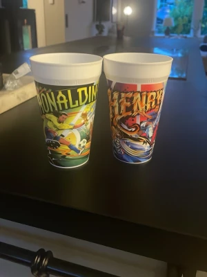 Ronaldinho och Henry mugg - Cool plastmugg med färgglatt tryck av en tecknad fotbollsspelare och texten 'ronAlDINHO'. Perfekt för drycker när du vill ha lite sportig känsla. Muggen är vit på insidan och har en konisk form.