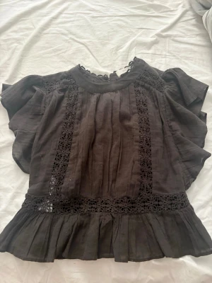 Brun blus med spets från MNG - Säljer en brun blus från MNG med vackra spetsdetaljer längs fram- och baksidan samt vid halsen. Blusen har korta, vida ärmar och volang nedtill. Perfekt för dig som gillar romantiska detaljer och en loose passform.
