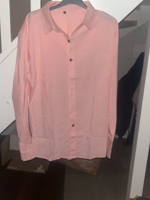 Ljusrosa skjorta i linne, stl M - Säljer en stilren ljusrosa skjorta i linne med klassisk krage och knäppning framtill. Skjortan har långa ärmar och en avslappnad passform, perfekt för en fräsch och trendig look.