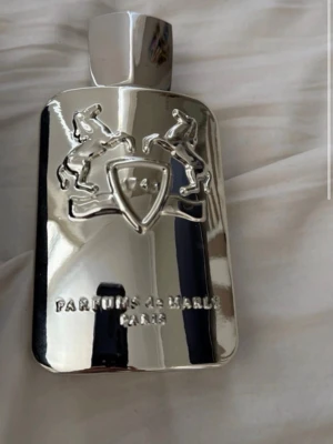Parfums de Marly Pegasus parfym - Exklusiv parfym från Parfums de Marly, modellen Pegasus. Flaskan är i spegelblankt silverfärgat material med reliefdetaljer av två hästar och sköld. Kommer i elegant svart förpackning med tydlig logga och text. En lyxig doft för dig som gillar unika parfymer.