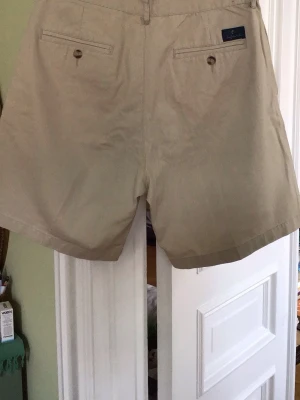 Beige klassiska shorts från OneWay - Snygga beige shorts från Polo Ralph Lauren med klassisk passform. De har två bakfickor med knappar och bälteshällor i midjan. Perfekta för varma dagar och enkla att matcha med olika stilar.