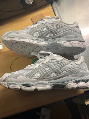 Vita ASICS Gel nyc - passar 41-43 /Säljer ett par fräscha vita ASICS sneakers med detaljer i ljusgrått. Skorna har en chunky sula, ovandel i mesh och syntetiskt skinn samt klassiska ASICS-loggor på sidorna. Perfekta för dig som gillar sportig och clean stil.