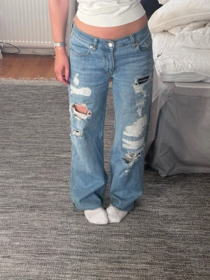 Ljusblåa baggy ripped jeans - Säljer ett par ljusblåa baggy jeans från Nelly med  slitningar och hål på båda benen. Jeansen har låg midja, midjemått 37 cm tvärs över. Jag är 164 och de är perfekt längd på mig. Skriv vid funderingar💕