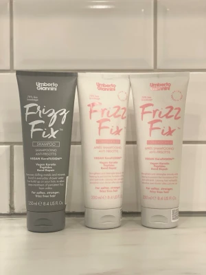 Umberto Giannini Frizz Fix set - Umberto Giannini Frizz Fix består av ett schampo i grå tub och två balsam i vita tuber. Alla produkter innehåller veganskt keratin och är speciellt framtagna för att motverka frissigt hår. Tubernas design är modern med tydlig text i vitt och rosa.
