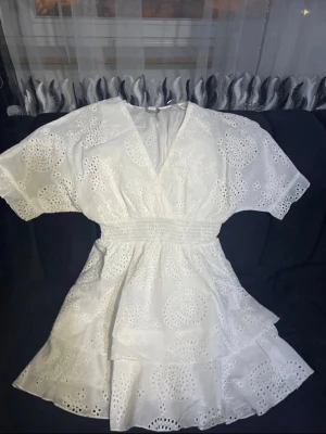 kort Klänningen  - Söt vit kortklänning med broderade detaljer och volangkant. Klänningen har v-ringning, korta ärmar och markerad midja med smock. Perfekt för sommarens alla tillfällen och ger en fräsch och romantisk look.