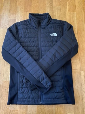 The North Face jacka vår/höst/vinter - Helt ny, använd en gång vid provning. Snygg svart quiltad jacka från The North Face med dragkedja framtill och hög krage. Jackan har långärmad design och diskret logga på bröstet. Perfekt för kyliga dagar och enkel att matcha med olika outfits.