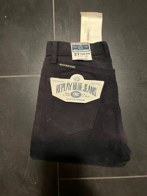 Svarta Replay Blue Jeans, raka ben - Snygga svarta jeans från Replay med raka ben och klassisk femficksdesign. Jeansen har en stor vit Replay Blue Jeans-logga på bakfickan och är tillverkade i ett slitstarkt denimtyg. Perfekta för dig som gillar en tidlös och clean look.