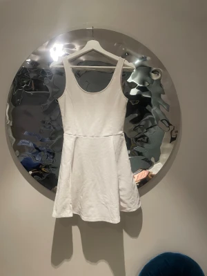 Vit ärmlös kortklänning i bomull - En enkel och stilren vit kortklänning i mjuk bomull. Klänningen är ärmlös med rundad halsringning och har en lätt utställd kjol som ger en avslappnad siluett. Perfekt för varma dagar och enkel att styla med accessoarer.