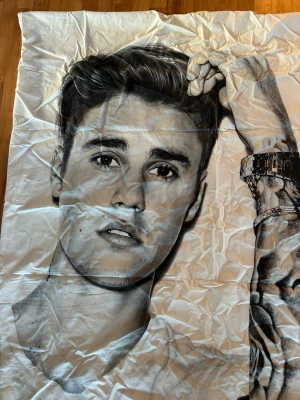 Justin Bieber påslakan med tryck - Stort vitt påslakan med svartvit tryck av Justin Bieber och hans tatueringar. Motivet visar hans arm med klocka och armband, samt hans namn skrivet längs sidan. Materialet är troligtvis bomull och designen är tydlig och ungdomlig.