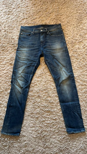 Mörkblå Tiger of sweden jeans - Säljer ett par mörkblå  jeans med snygga slitningar och tvättade detaljer. Klassisk femficksmodell med knappgylf och läderpatch bak i midjan. Från tiger of sweden med riktigt snygg tvätt storlek 31/32