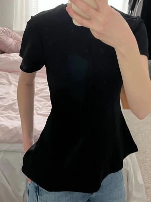 Svart figurnära topp från H&M  - Säljer denna svarta, figurnära topp från H&M med korta ärmar och rund halsringning. Toppen är utsvängd nere och har fina sömmar som går ner på båda sidorna av toppen! Superfin kostymliknande känsla! 