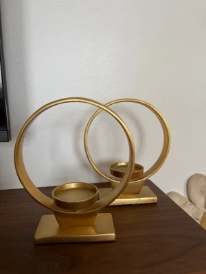 Guldfärgade ljushållare i metall - Två stilrena ljushållare i guldfärgad metall med rund design och fyrkantig fot. Perfekta som dekoration på bord eller hylla för att skapa en mysig känsla. Passar till värmeljus och har en modern, minimalistisk look.