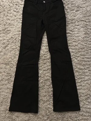 Svarta bootcut jeans - Säljer ett par svarta bootcut jeans med klassisk femficksdesign och knappgylf. Jeansen har utsvängda ben och är tillverkade i ett mjukt denimtyg som ger en snygg siluett. Perfekta för dig som gillar en retroinspirerad look.