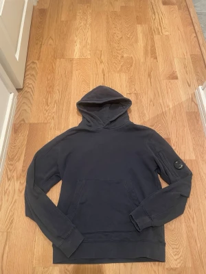 C.p.company hoodie - En snygg c.p.company hoodie i mörkblå. Den har en repa på själva c.p.company knappen men den synns inte märkvärdigt mycket. Pris kan diskuteras. Den passar runt 165-175