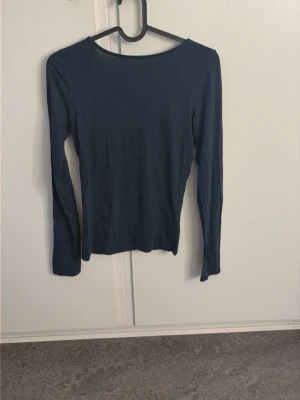 Mörkblå långärmad topp - En enkel och stilren mörkblå långärmad topp med rund halsringning fram och djupare urringning i ryggen. Toppen har en tight passform och är tillverkad i ett mjukt, stretchigt material som känns bekvämt mot huden.