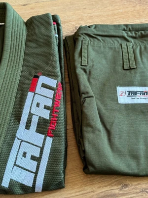 Grön BJJ gi från Tafan Fightwear A3  - Maskerad- eller cosplaydräkt inspirerad av kampsport, i militärgrönt ripstop-material. Setet består av jacka och byxa med broderad TAFAN-logga i vitt och rött på jackan samt patch på byxan. Perfekt för dig som vill klä ut dig till fighter eller kampsportare. Available sizes are A3,M1,M3,M4. Coat with Pearl Weave 450 GSM Pant with ripstop 10 Oz Check Picture of Size Chart 🤙 Check Size Chart on Pictures.. Quality Product.