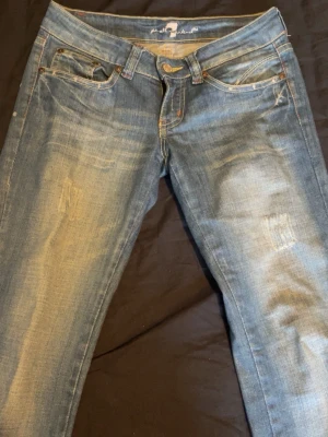 Blå slitna jeans med raka ben - Säljer ett par blå jeans med slitningar, raka ben och som är jättelåga i midjan. Jeansen har klassisk femficksmodell, låg midja och ljusa tvättade partier framtill. Perfekta för en avslappnad och trendig look.